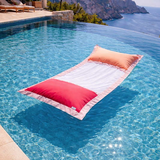 chillisy Wasserhängematte Menorca II in Rosa, Apricot und Pink Grapefruit schwimmt in einem luxuriösen Infinity Pool mit Meerblick – Premium Wasser Lounger für Pool, Meer und See.