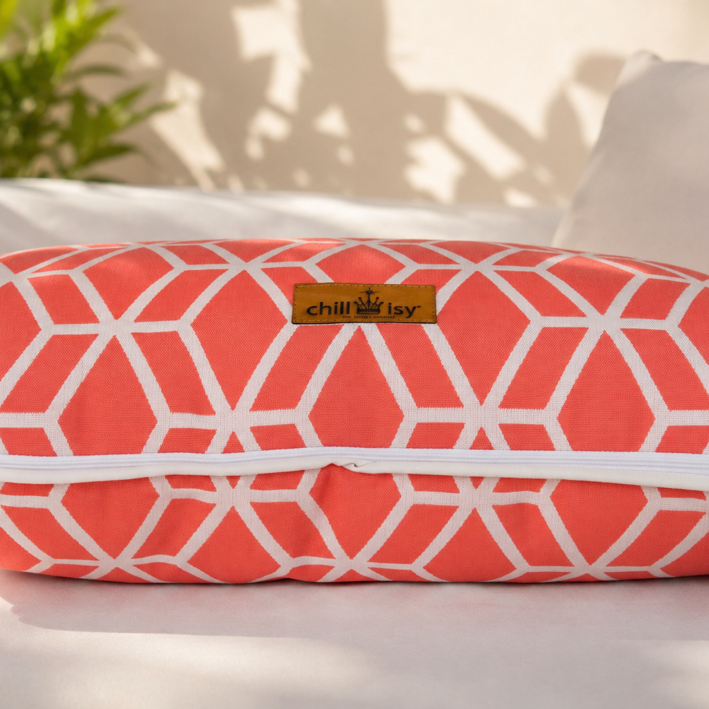 Designer-Kissen Crystal Gold von chillisy® in Koralle mit weißem geometrischem Muster, weißem Keder und Goldlabel auf einer stilvollen Outdoor-Lounge.