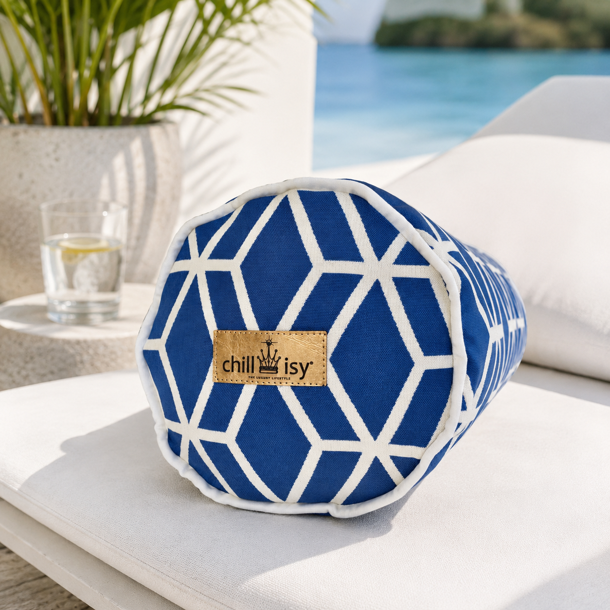 Blaue Designer-Nackenrolle Crystal Gold von chillisy® mit weißem geometrischem Muster, weißem Keder und Goldlabel auf einer stilvollen Sonnenliege am Pool.
