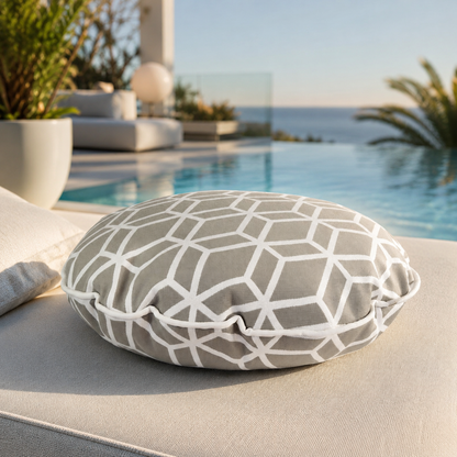 chillisy® Designer-Rundkissen Crystal Gold Hellgrau mit weißem geometrischem Muster, weißem Keder und Goldlabel auf einer luxuriösen Outdoor-Lounge mit Infinity-Pool und Meerblick – Premium Outdoor-Kissen, genäht in Deutschland