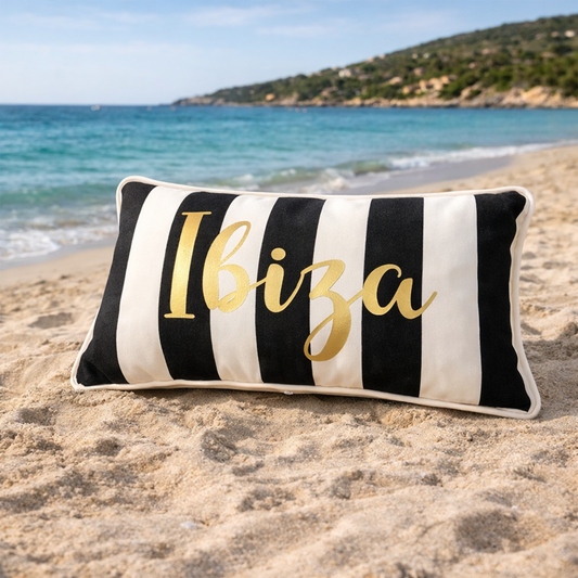 Ibiza Kissen Schwarz Weiß gestreift mit goldenem Aufdruck für Outdoor und Indoor, hergestellt von chillisy in Deutschland - im Sand am Strand mit Meer im Hintergrund.