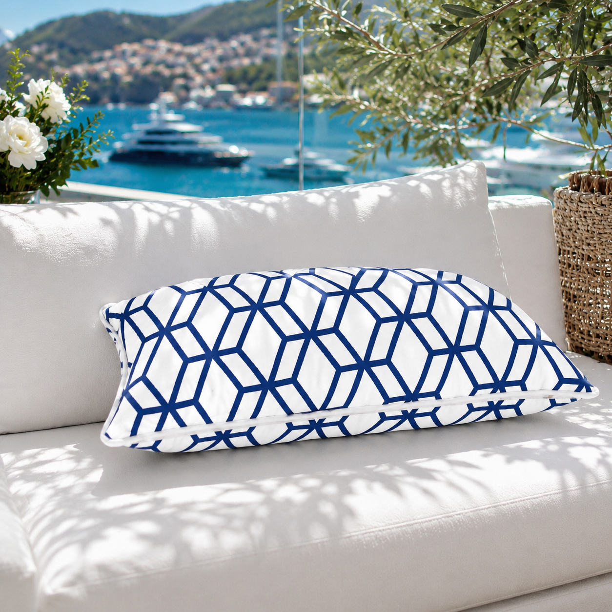 Luxuriöses Outdoor-Dekokissen mit weißem Grundstoff und marineblauem geometrischem Muster auf einer eleganten weißen Gartenlounge mit Meerblick. Das Kissen besitzt einen weißen Keder und das goldene chillisy®-Label und ist handgefertigt in Deutschland – ideal für Terrasse, Garten und Lounge.