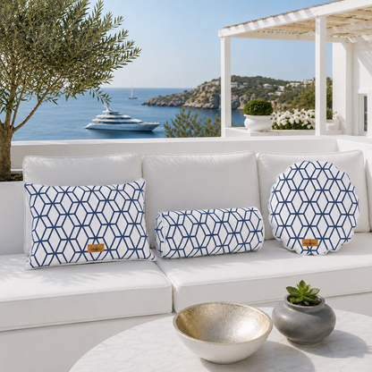 Exklusive Outdoor-Kissen-Kollektion von chillisy® auf einer weißen Luxus-Gartenlounge mit Meerblick. Rechteckiges Dekokissen, Nackenrolle und rundes Kissen mit weißem Stoff, marineblauem geometrischem Muster, weißem Keder und goldenem chillisy®-Label – stilvoll inszeniert vor einer mediterranen Küstenlandschaft mit Yacht.

