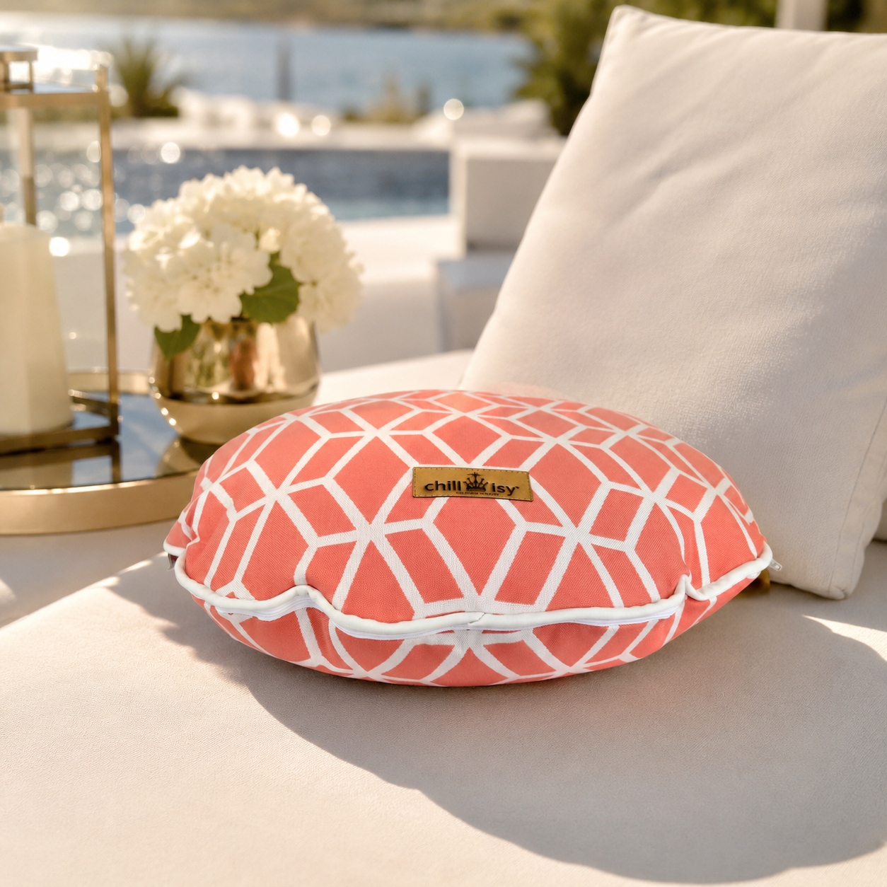 Korallenfarbenes Designer-Rundkissen Crystal Gold von chillisy® mit weißem geometrischem Muster und Goldlabel auf einer stilvollen Pool-Lounge.