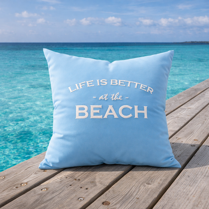 Dekokissen Aqua Blau mit weißer Stickerei LIFE IS BETTER AT THE BEACH auf Holzsteg am Meer