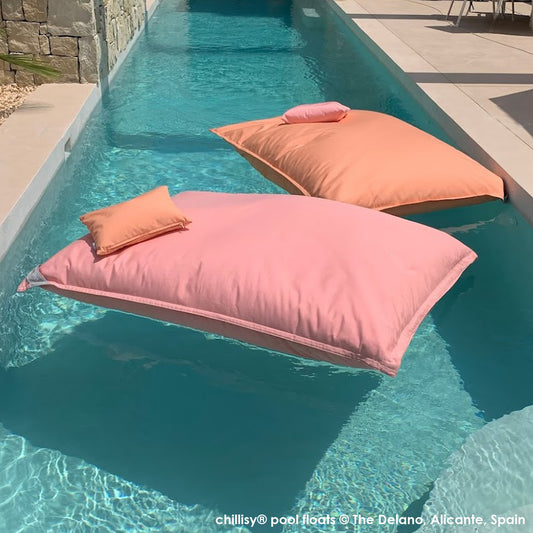 Zwei Pool Sitzsäcke in Rosa und Apricot von chillisy schwimmen auf langem türkis farbenen Pool zwischen beigen Terrassenböden - Poolkissen made in Germany by chillisy. Foto: Delano Ferienhaus Spanien