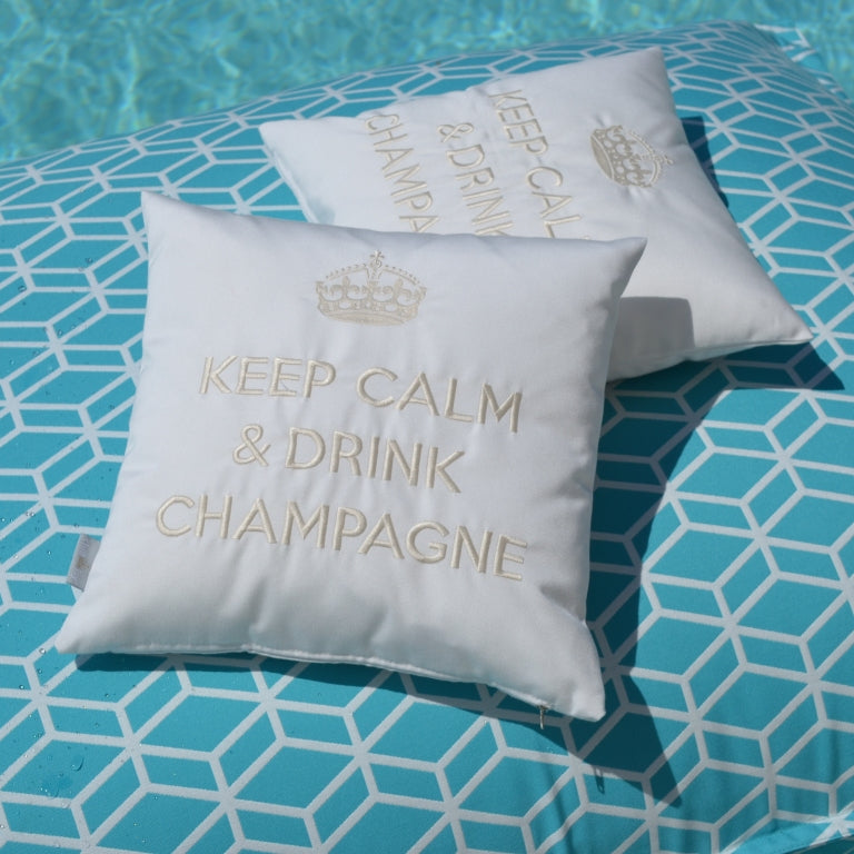 Zwei Dekokissen KEEP CALM & DRINK CHAMPAGNE in weiß wollweiss mit Krone bestickt auf türkisem Poolkissen.