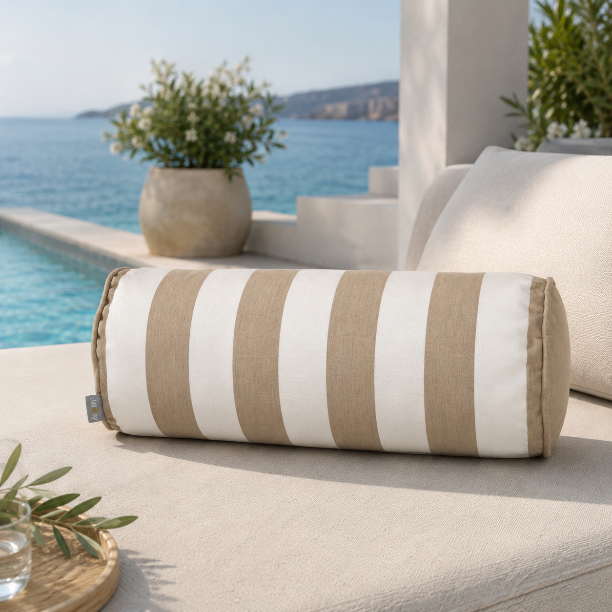Luxuriöse Outdoor-Nackenrolle in Beige-Weiß mit breiten Blockstreifen auf einer eleganten Lounge am Pool. Die 50 cm lange und 20 cm starke chillisy® Nackenrolle ist aus hochwertigem Outdoorstoff gefertigt, UV-beständig, farbecht und Made in Germany.
