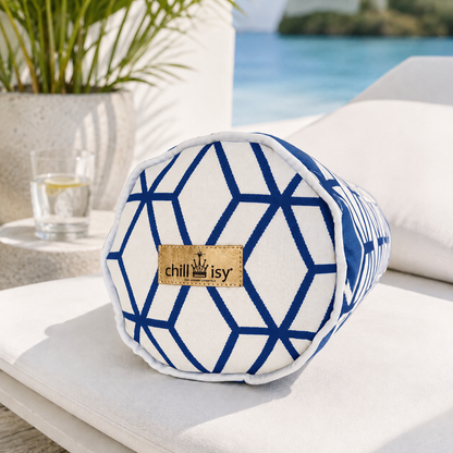 Weiße Outdoor-Nackenrolle mit blauem geometrischem Design, weißem Keder und chillisy® Goldlabel auf einer luxuriösen Sonnenliege am Mittelmeer. Mediterrane Küstenlandschaft mit türkisblauem Wasser, Natursteinmauer und Olivenbaum schafft ein exklusives Outdoor-Ambiente.