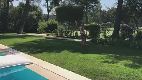 Mädchen macht Fklickflack auf das weiße Poolkissen von chillisy das im Pool schwimmt.
