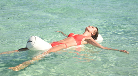 Frau entspannt auf einer weißen XXL-Schwimmnudel Super Maccheroni von chillisy® im kristallklaren Wasser. Die luxuriöse Poolrolle stützt Kopf, Rücken und Beine und sorgt für schwerelosen Liegekomfort im Pool.